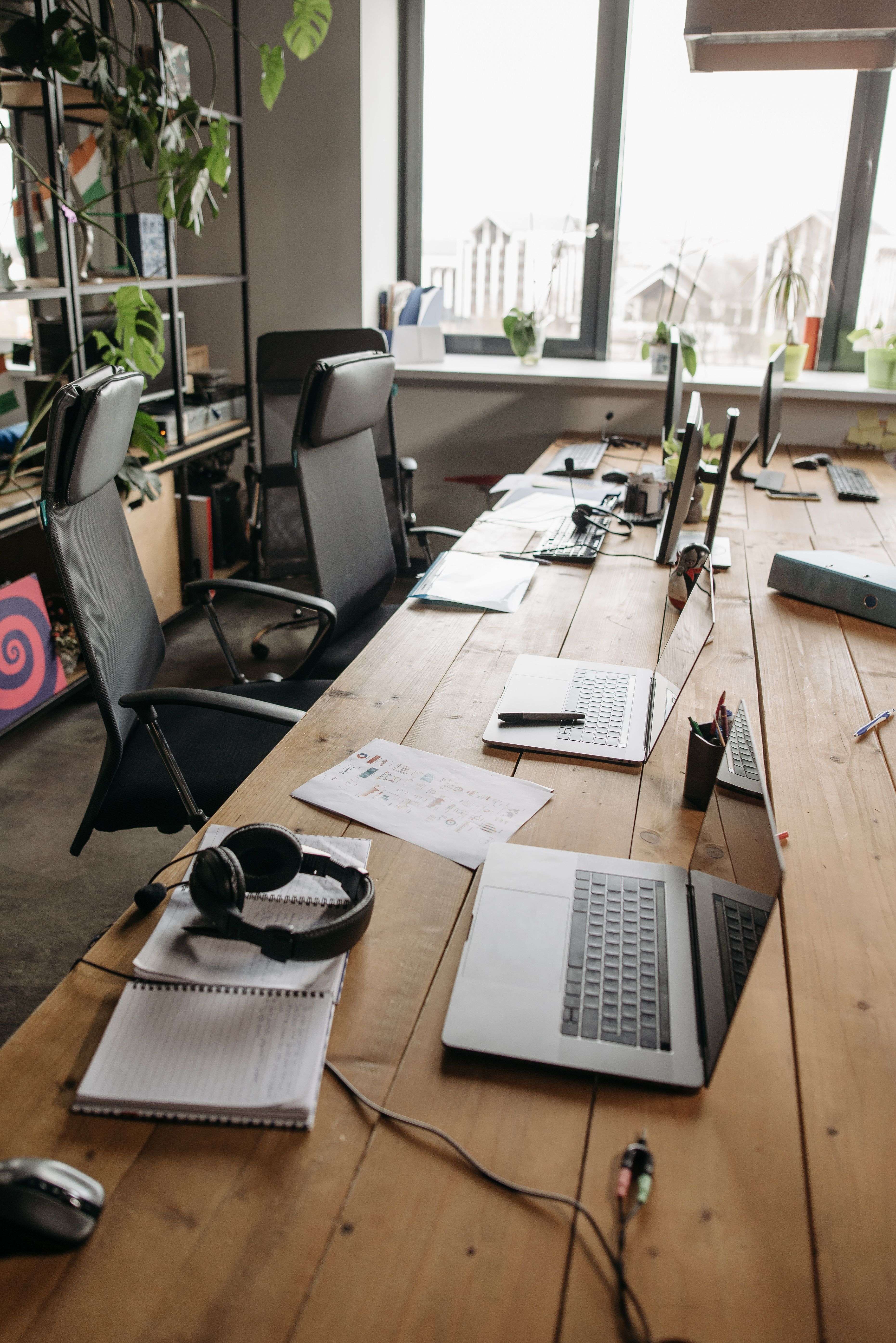 The workspace — a long wooden desk with laptops, headphones and notebooks by the window